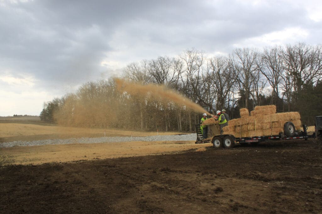Workers spreading hay debris across a plot of land